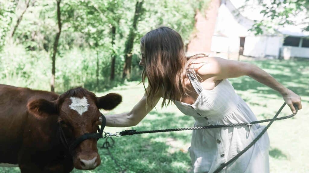 women wearing dress holding a rope in one hand and petting a calf with the other