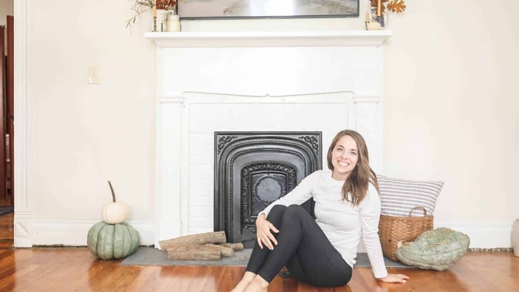 women sitting in front of a white DIY faux fireplace with pumpkins around on the floor