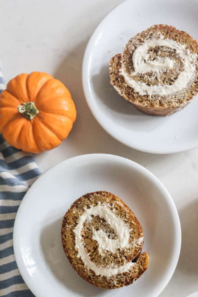 two slices of sourdough pumpkin rolls on white plates with a orange small pumpkin to the left