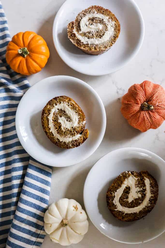 three slices our sourdough pumpkin rolls on white plates with pumpkins spread around