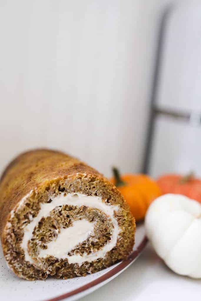 sourdough pumpkin roll with cream cheese filling on a white plate with orange and white pumpkins to the right