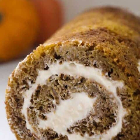 sourdough pumpkin roll with cream cheese frosting rolled into a log and placed on a white plate