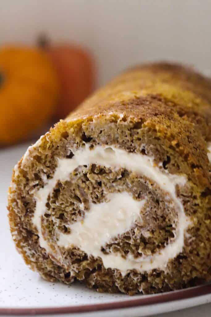 sourdough pumpkin roll with cream cheese frosting rolled into a log and placed on a white plate