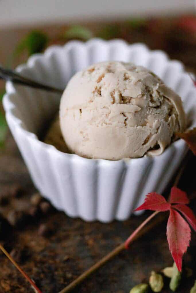 One white bowl with one scoop of chai ice cream with a spoon.
