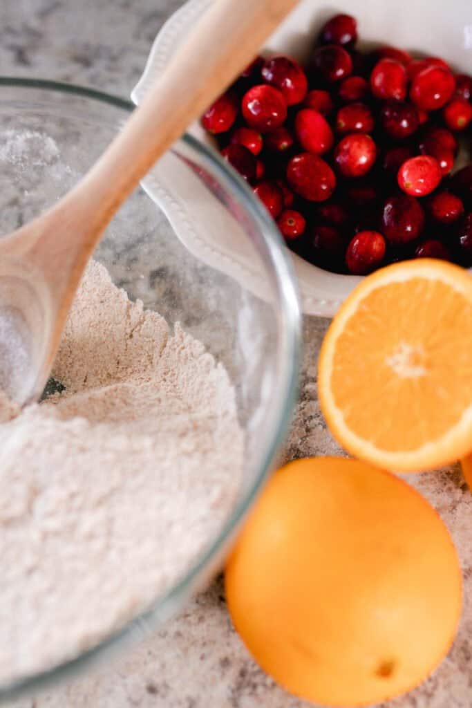 bowl of dry ingredients with sliced oranges and a bowl of cranberries behind