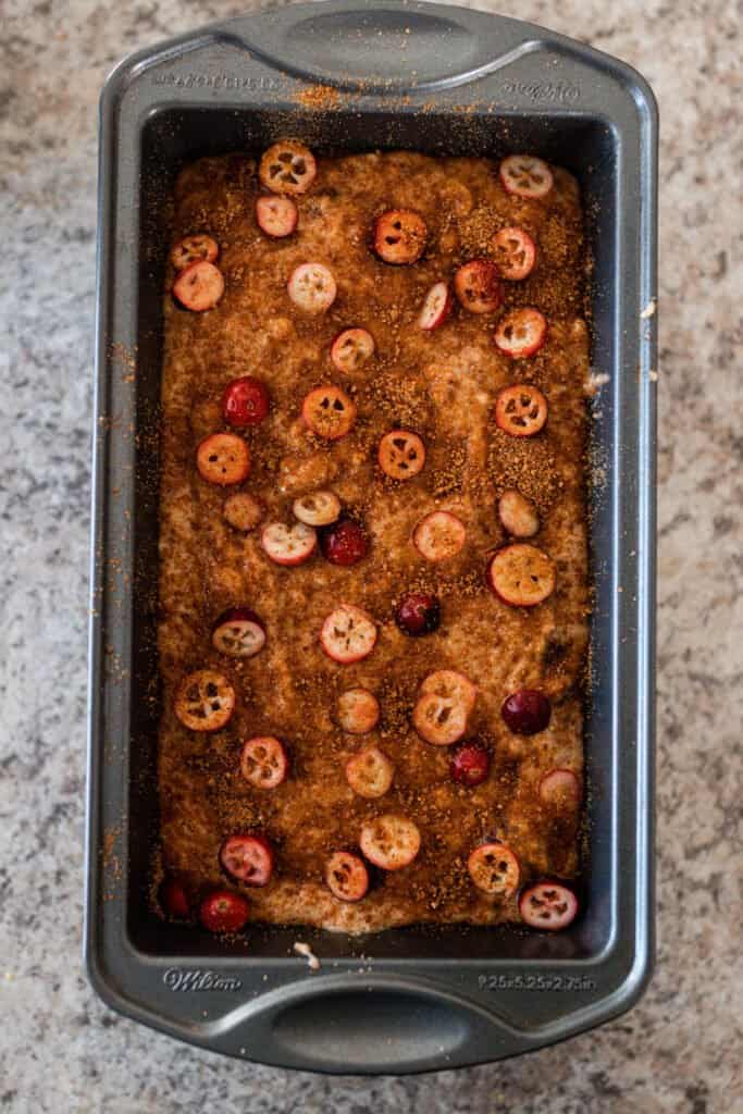 sliced cranberries and coconut sugar on top of sourdough cranberry bread batter in bread pan