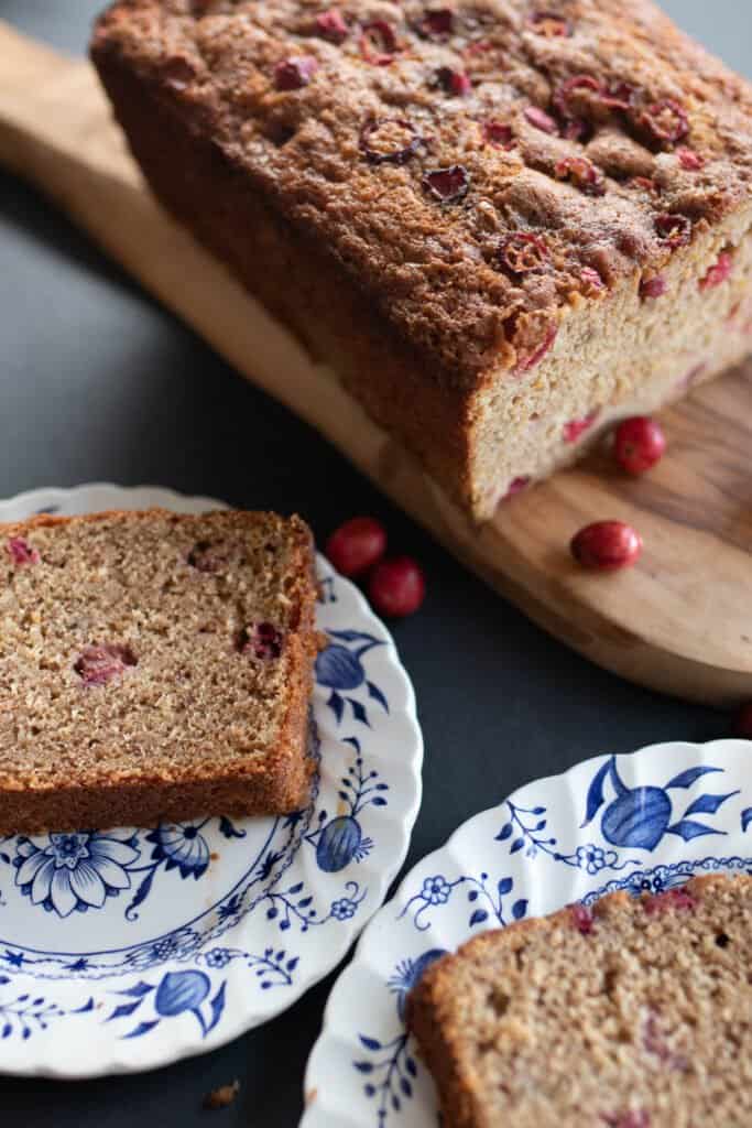 sourdough cranberry bread slices on two white and blue plates. The remaining bread is on a wood cutting board in the background