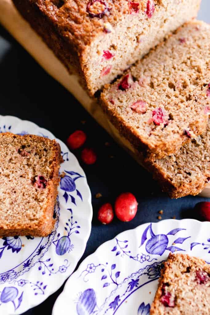 sourdough orange cranberry bread sliced on a wood cutting board with two white and blue plates with slices of bread.