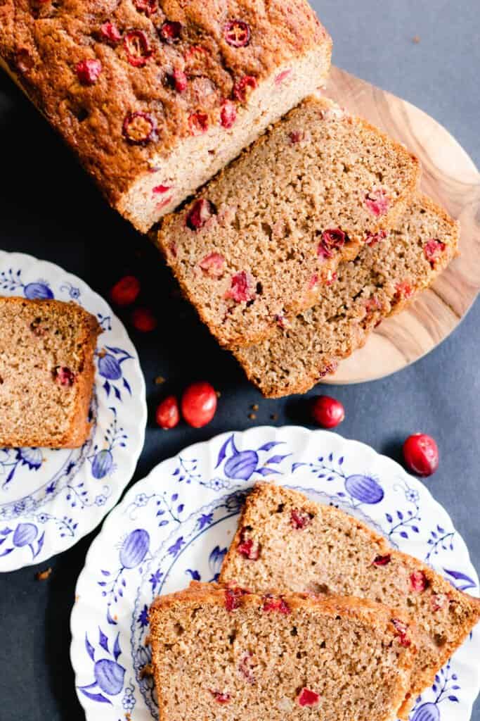 Cranberry orange quick bread on two white and blue plates with the loaf on a cutting board