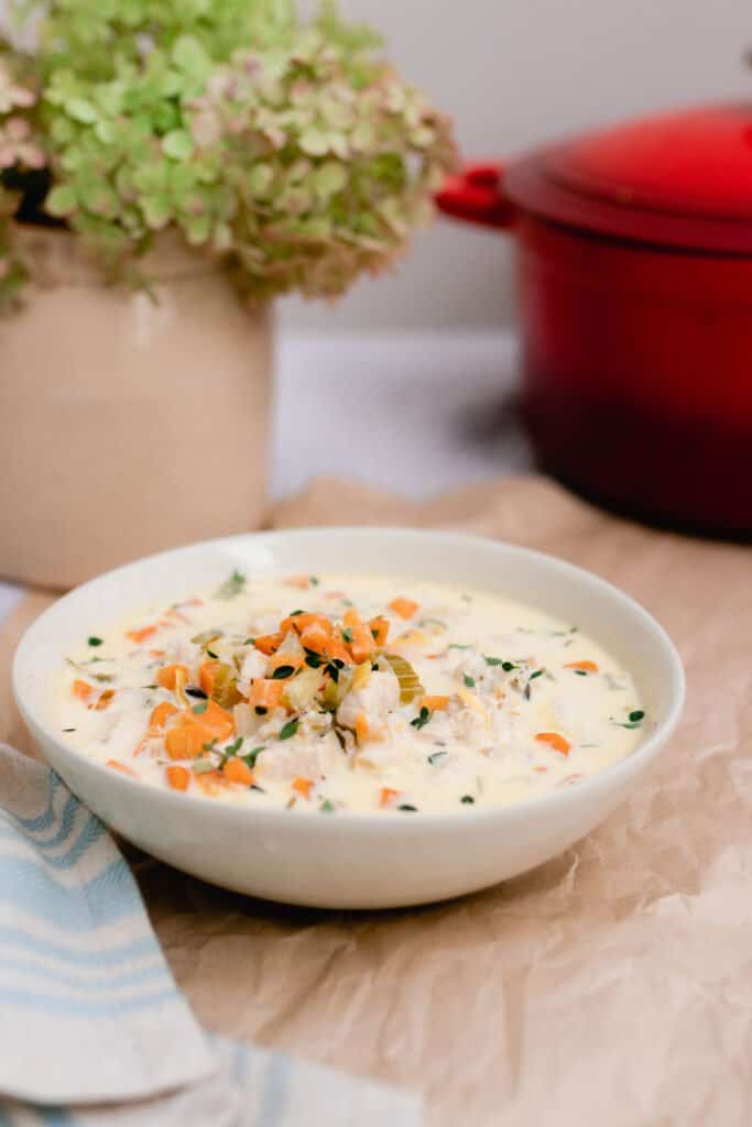 bowl of creamy chicken and wild rice soup with vegetables on a wooden table with a vase of hydrangeas and a red dutch oven in the background