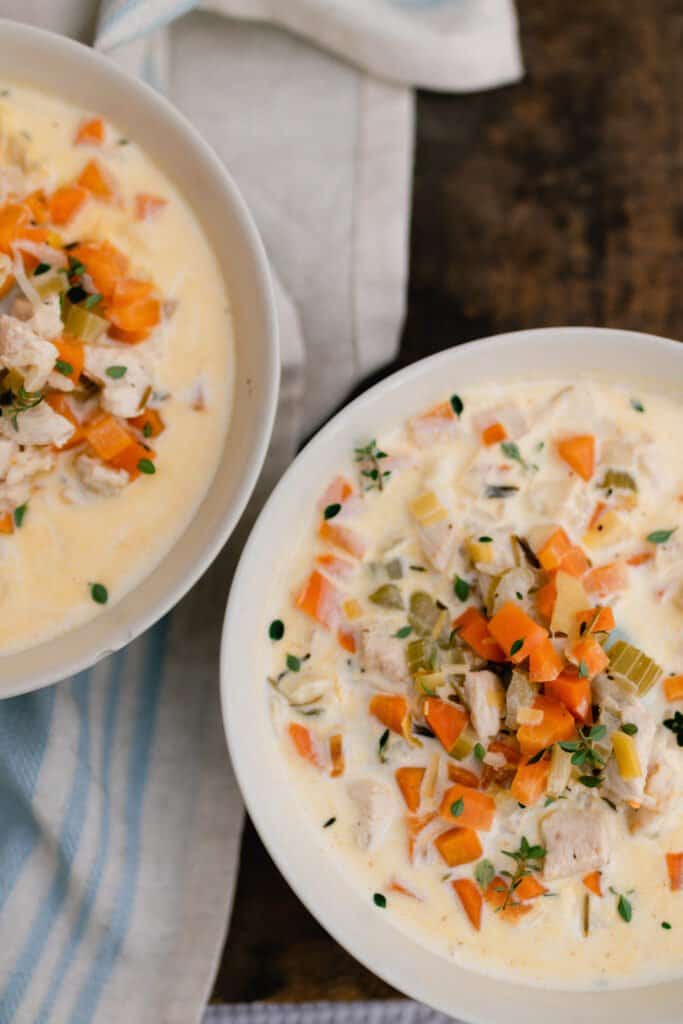 two bowls of creamy chicken and wild rice soup on a blue and cream stripped towel