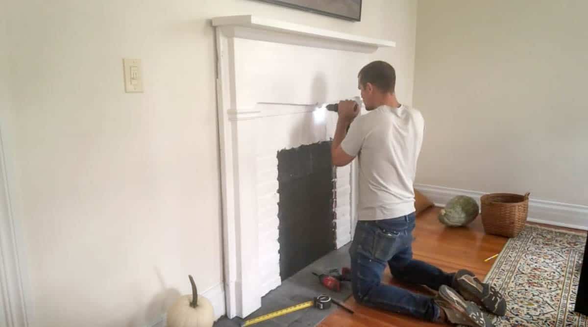 man securing faux fireplace to the wall with screws