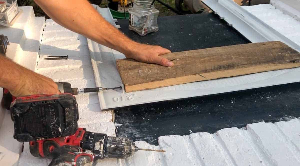 man drilling 1x6 to the back of a fireplace insert