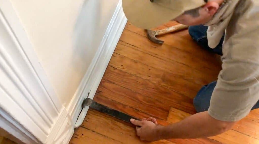 man removing shoe molding from base boards
