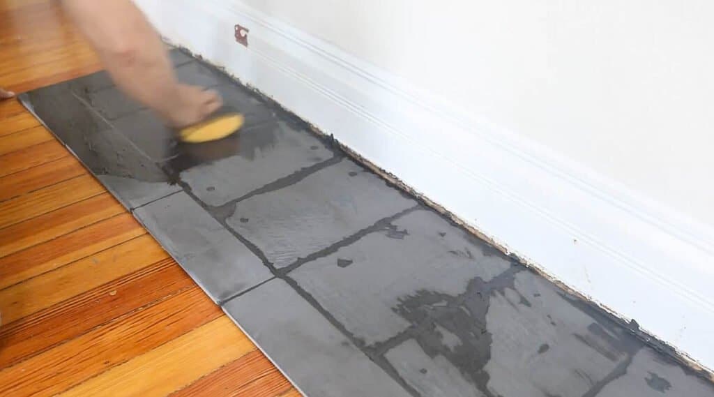 man wiping excess grout off with a wet sponge