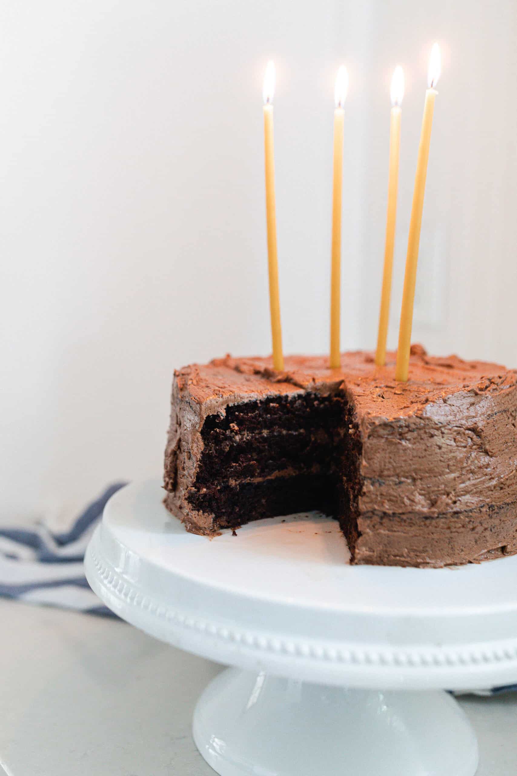 sourdough chocolate cake with chocolate frosting and 4 long beeswax candles on a white cake stand