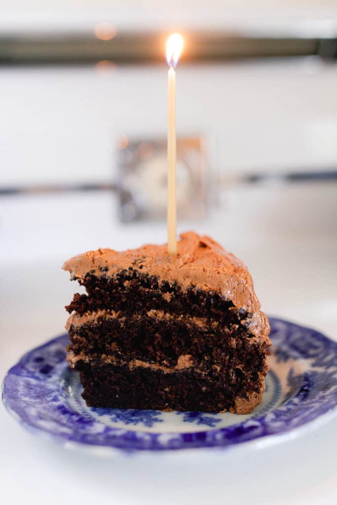 slice of sourdough chocolate cake with chocolate frosting on a blue and white plate on a vintage 1940s stove