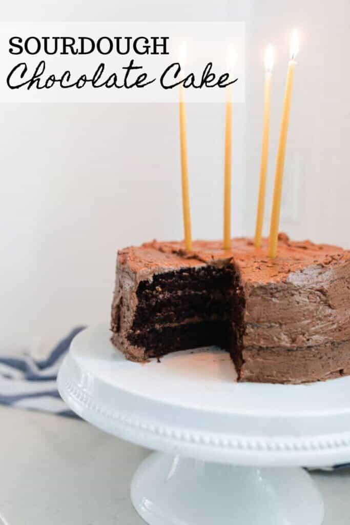 sourdough chocolate cake with chocolate frosting and 4 long beeswax candles on a white cake stand