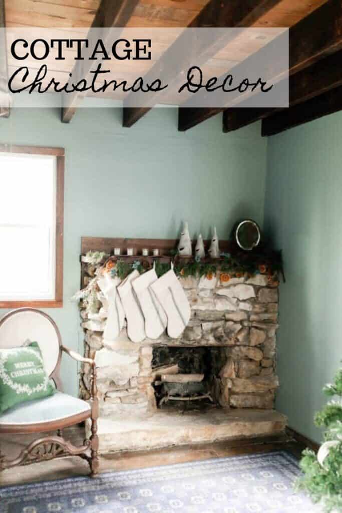 stone fireplace mantle hung with garland and stockings with a vintage chair with a Christmas pillow to the left