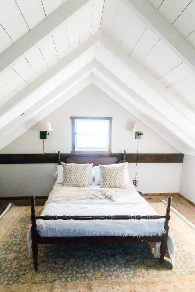 upstairs of a cottage painted white with a antique bed covered in a comfy quilt and vintage pillows