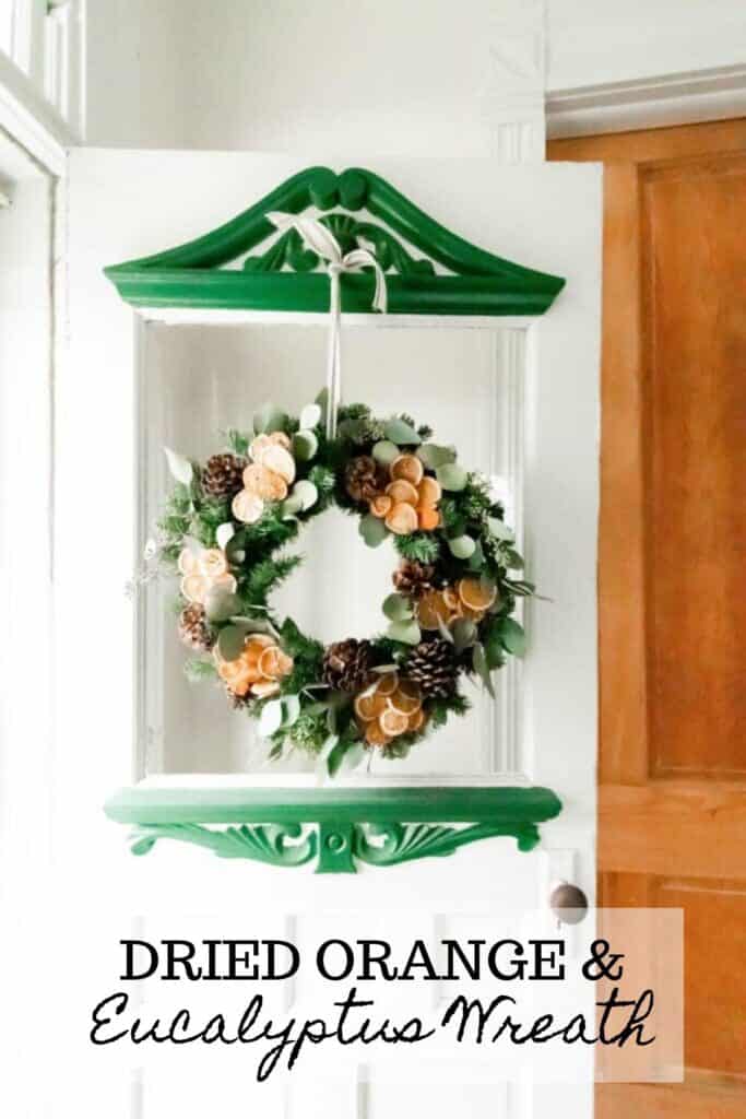 Dried eucalyptus wreath with sliced dried oranges and pinecones hanging with ribbon on a vintage white and green door