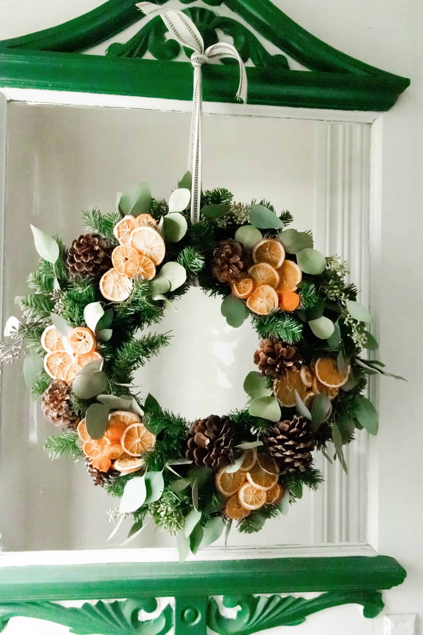 Dried orange and eucalyptus Christmas wreath hanging on a vintage white and green door with glass