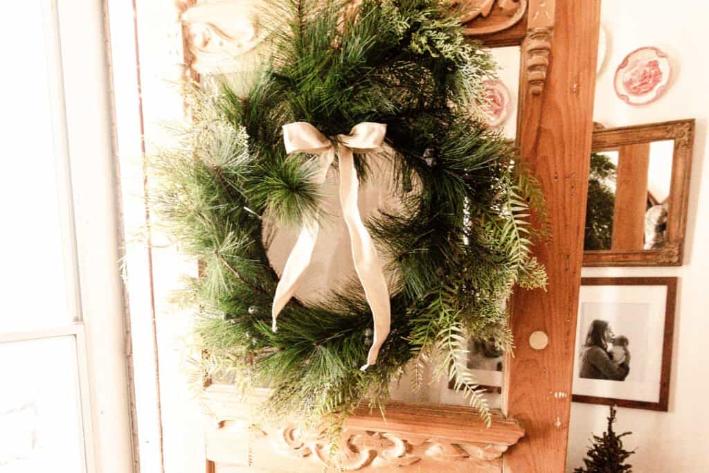 greenery wreath with a cream colored bow hung on a antique wood door