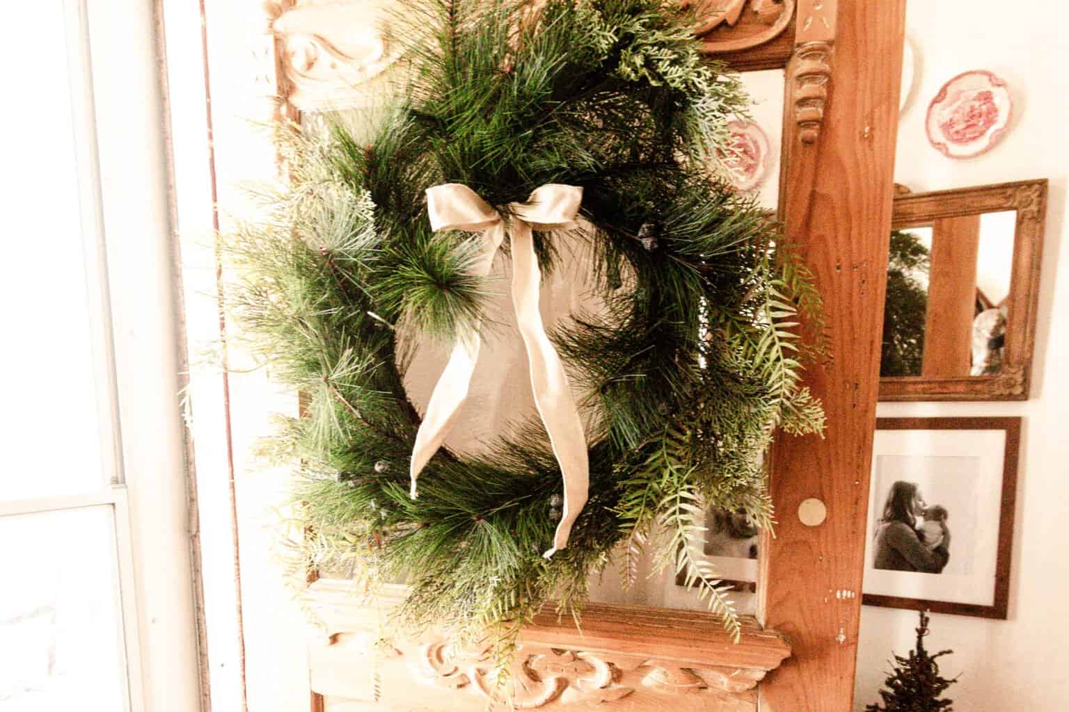 greenery wreath with a cream colored bow hung on a antique wood door