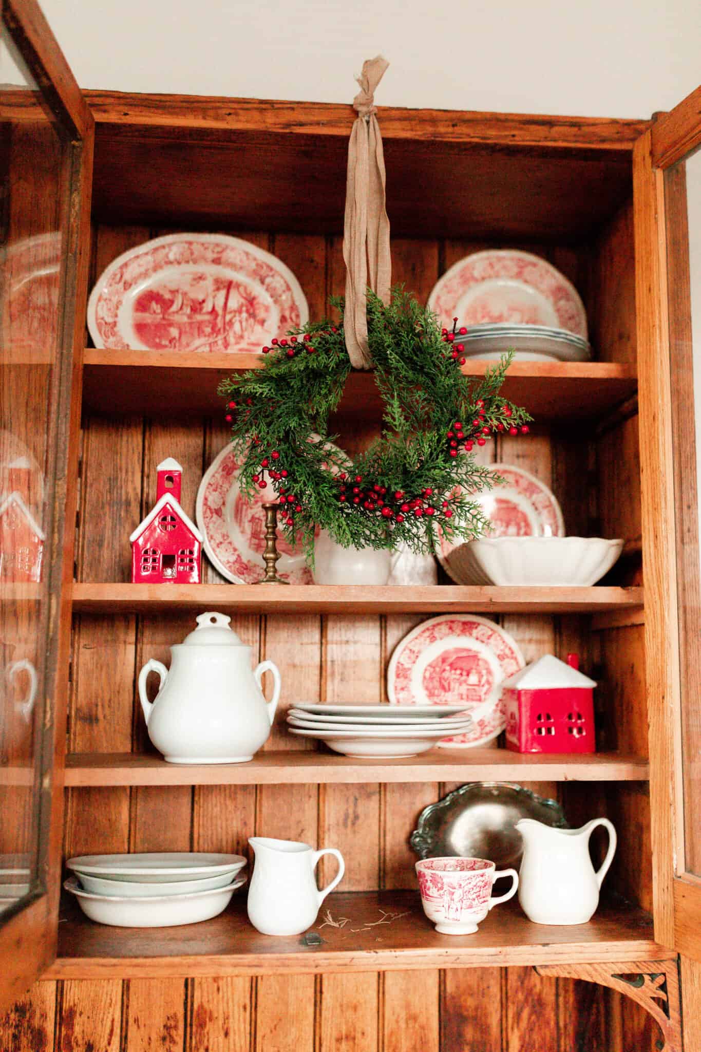 red and white vintage plates, white vases, and small red and white Christmas houses in a wood cabinet