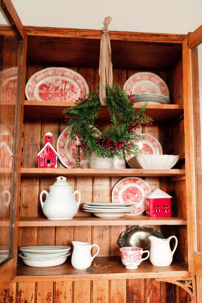 red and white vintage plates, white vases, and small red and white Christmas houses in a wood cabinet