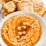 roasted red pepper hummus in a bowl drizzled with olive oil. Sourdough flat bread is in the background