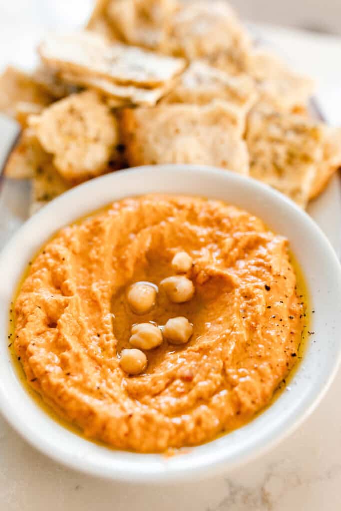 roasted red pepper hummus in a bowl drizzled with olive oil. Sourdough flat bread is in the background