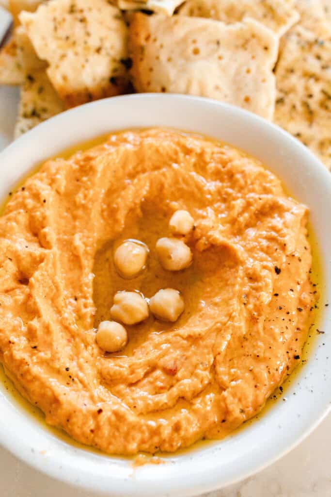 close up of red pepper hummus topped with chickpeas in a white bowl