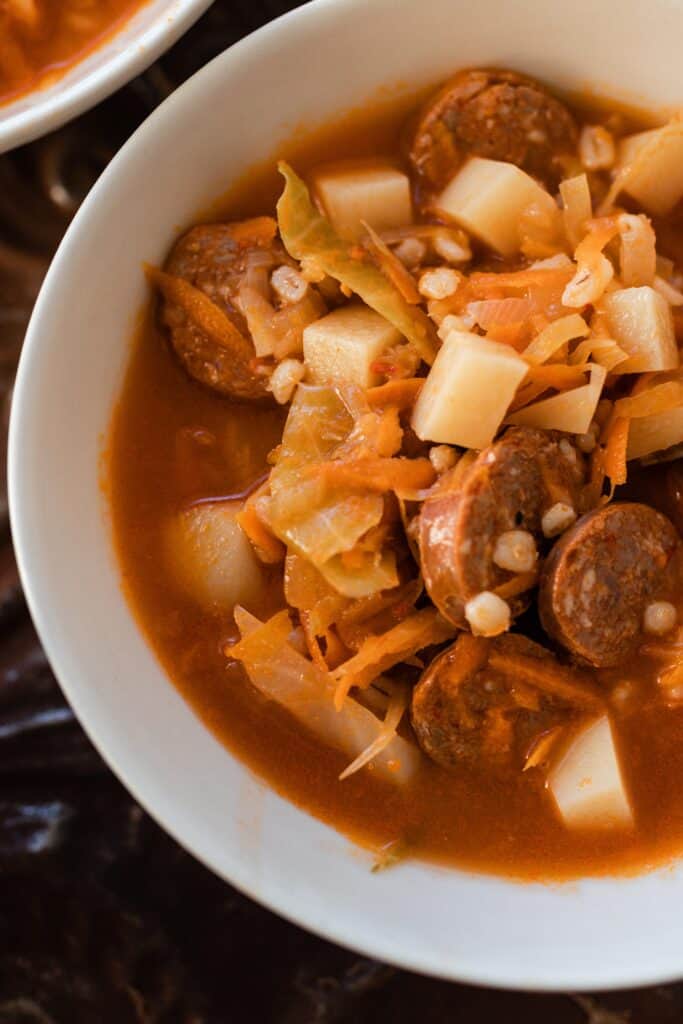 close up of sausage sauerkraut soup in a white bowl