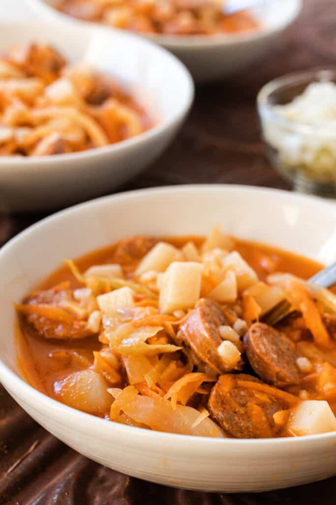 side view of a white bowl of sausage sauerkraut soup