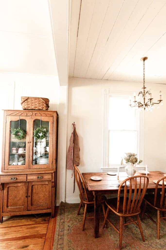 eat-in kitchen with wreaths hanging with ribbon from a vintage China cabinet, a red and white checked apron hung on the wall and a table set with red and white plates