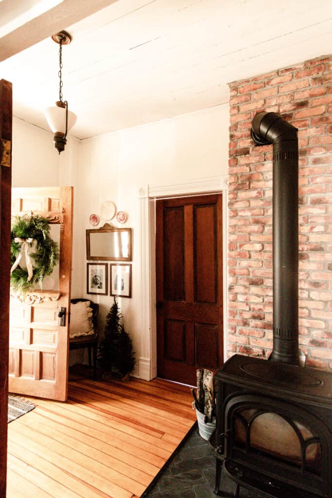 farmhouse entryway decorated for Christmas with a wreath hanging from the front door and small Christmas trees next to the chair