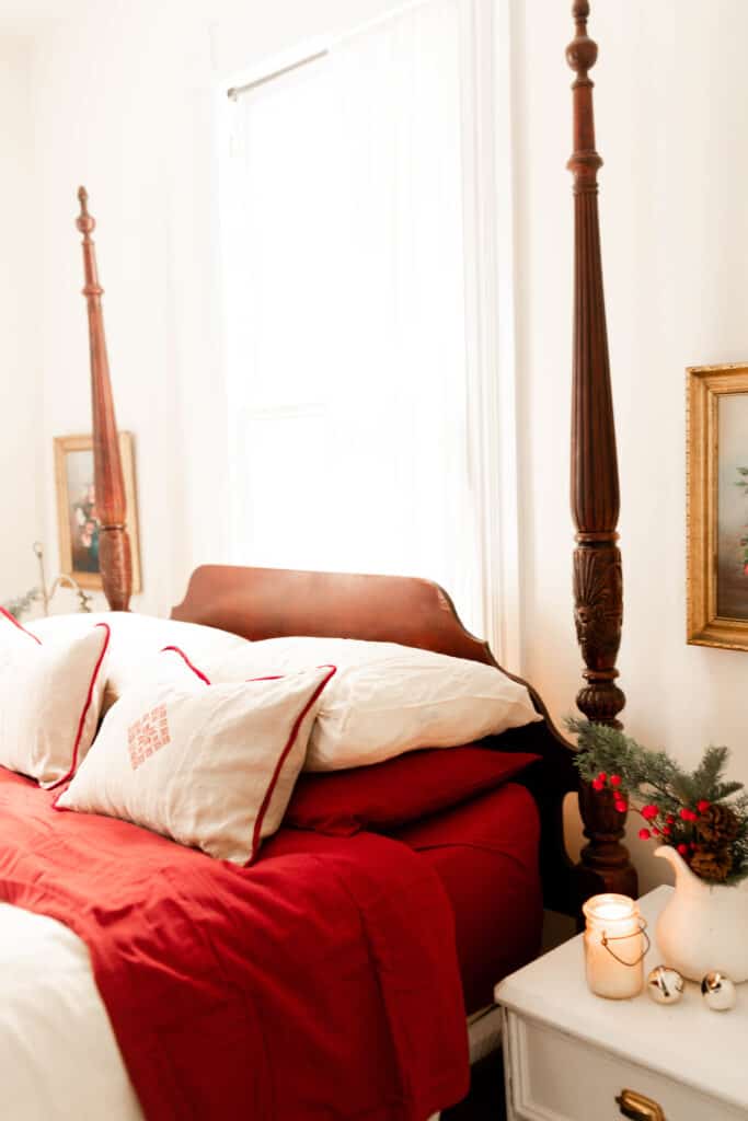 victorian bed with red and white linens. While linen pillows with red piping and a red decal in the middle sit on top of the bed