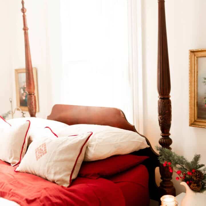 victorian bed with red and white linens. While linen pillows with red piping and a red decal in the middle sit on top of the bed