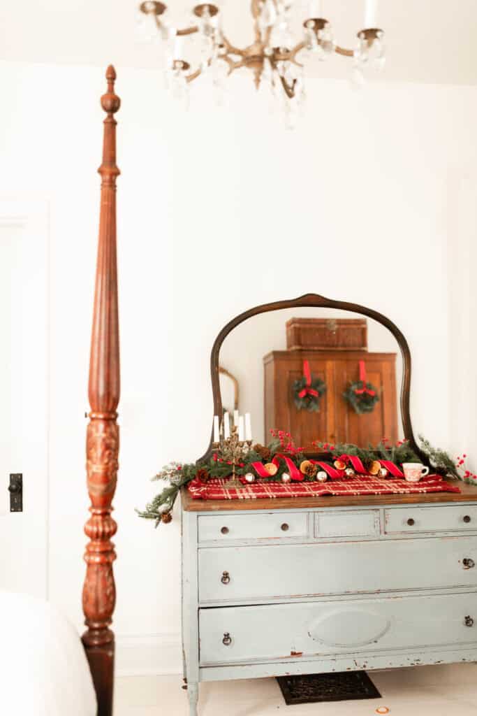 antique blue dresser decorated for Christmas with a red plaid runner, garland, red and gold ribbon, and bells