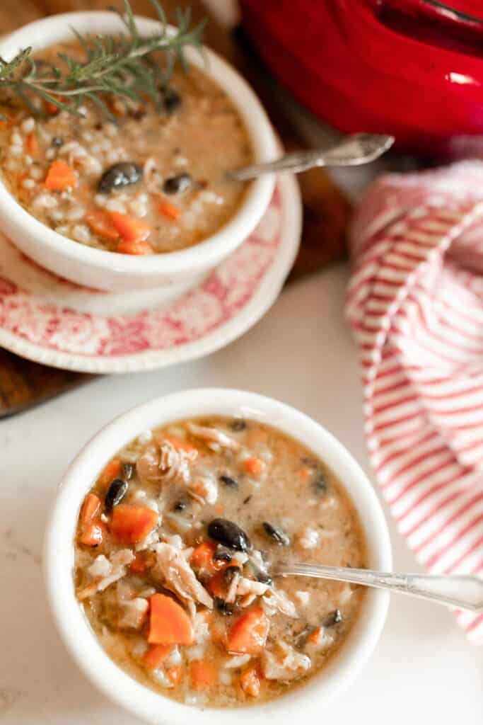 two bowls of chicken Marsala Soup. A red dutch oven and red and white stripped towel sit in the background