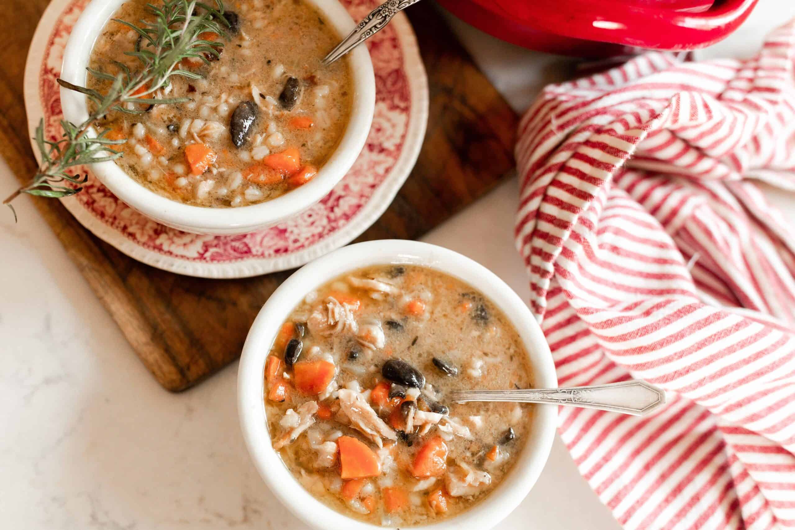 two bowls of chicken Marsala Soup. One bowl is on a red and white antique dish on top a wooden cutting board. A red and white stripped towel sits to the right