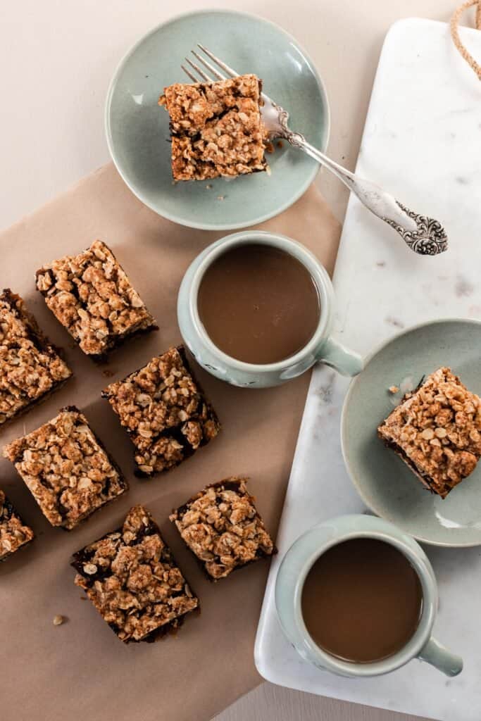 overhead photo of date squares on parchment paper with two mugs of coffee. 