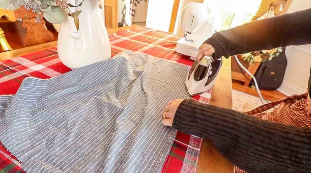 women wearing a gray sweater folding over and ironing blue and white stripped fabric to create a hem
