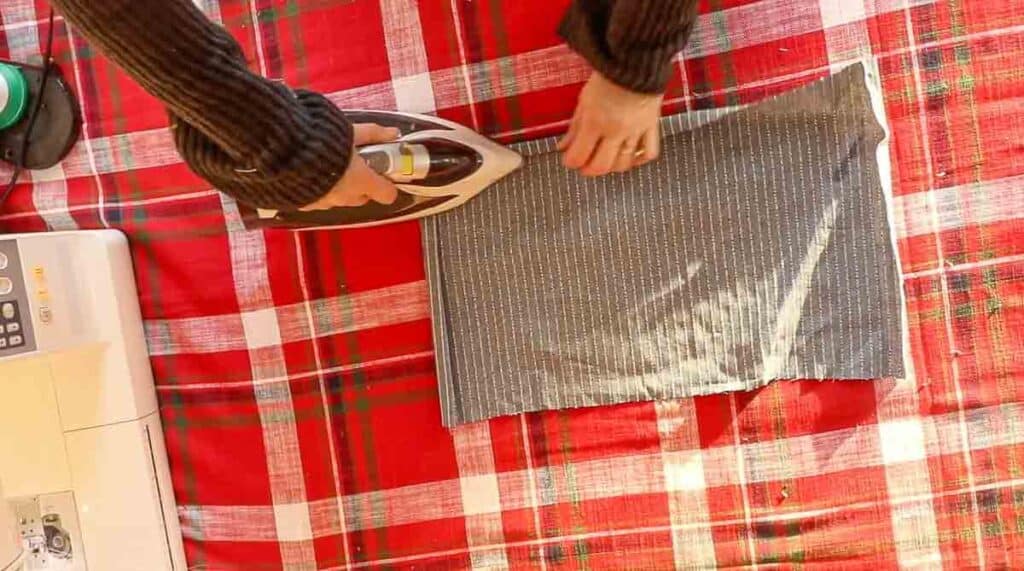 women folding over fabric and ironing a hem over to create a pocket.