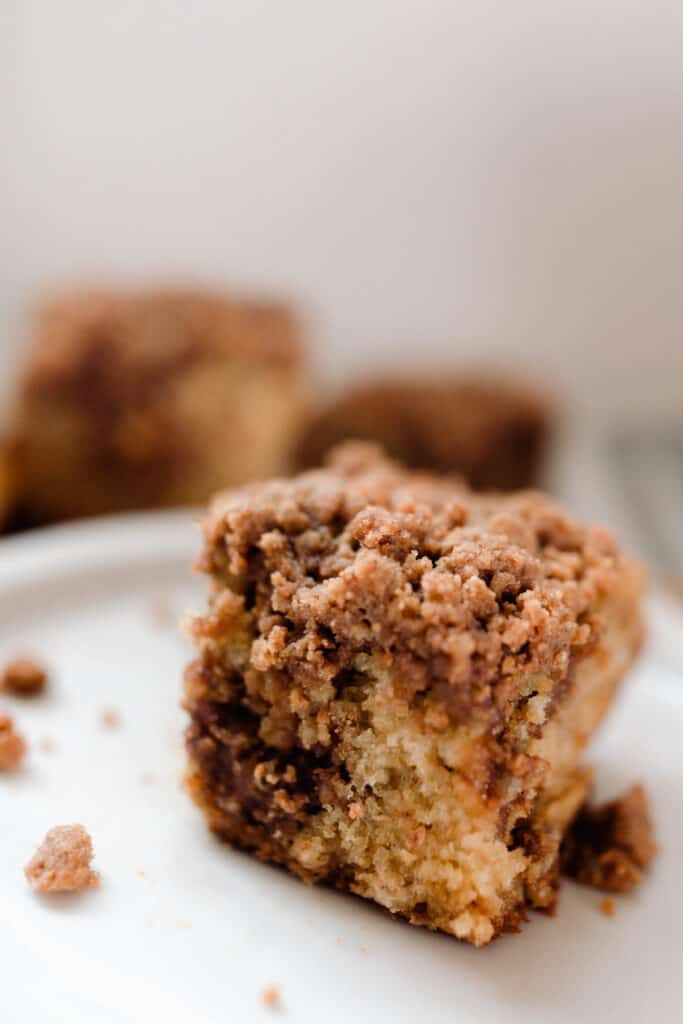 square of sourdough coffee cake on a white plate with more cake in the background