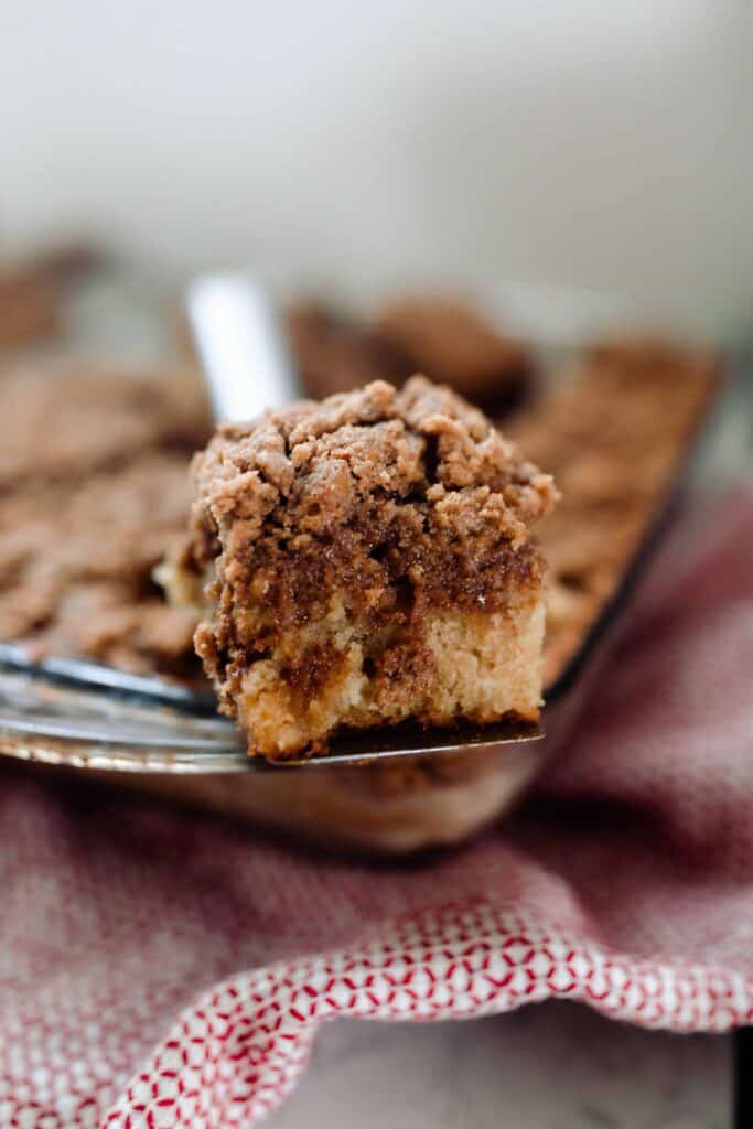 slice of coffee cake resting on top of baking dish of cake on a red and white towel