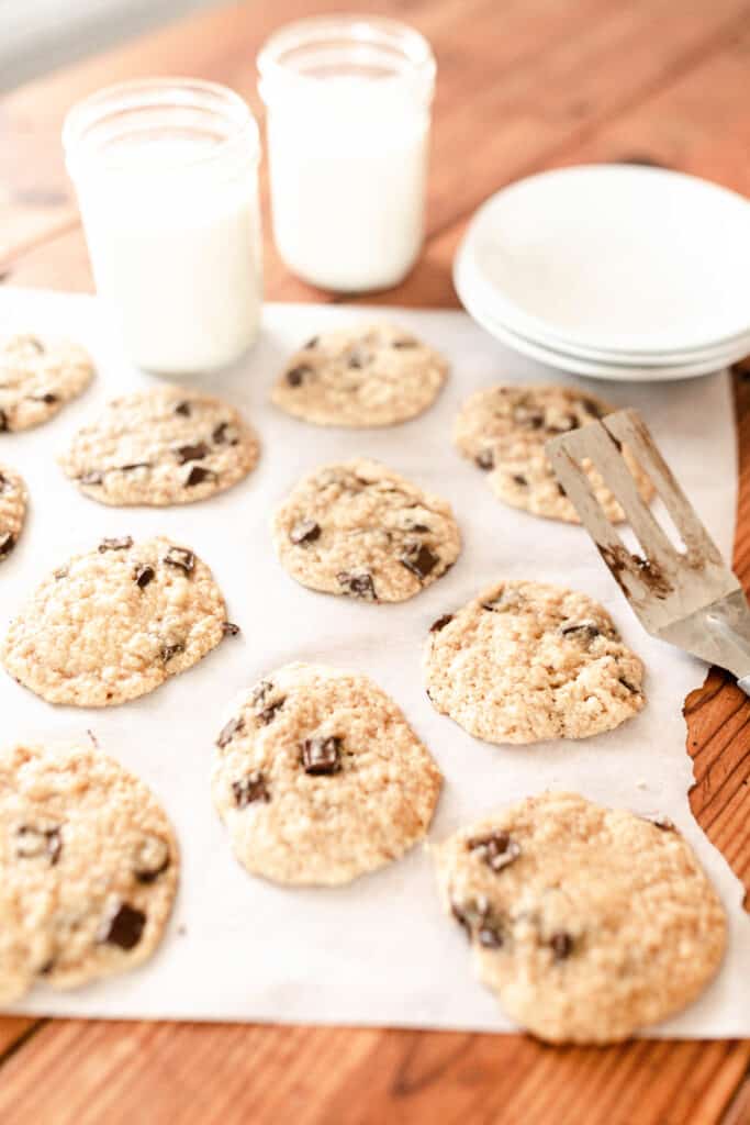 sourdough cookies on parchment paper with glasses of milk ad plates in the back