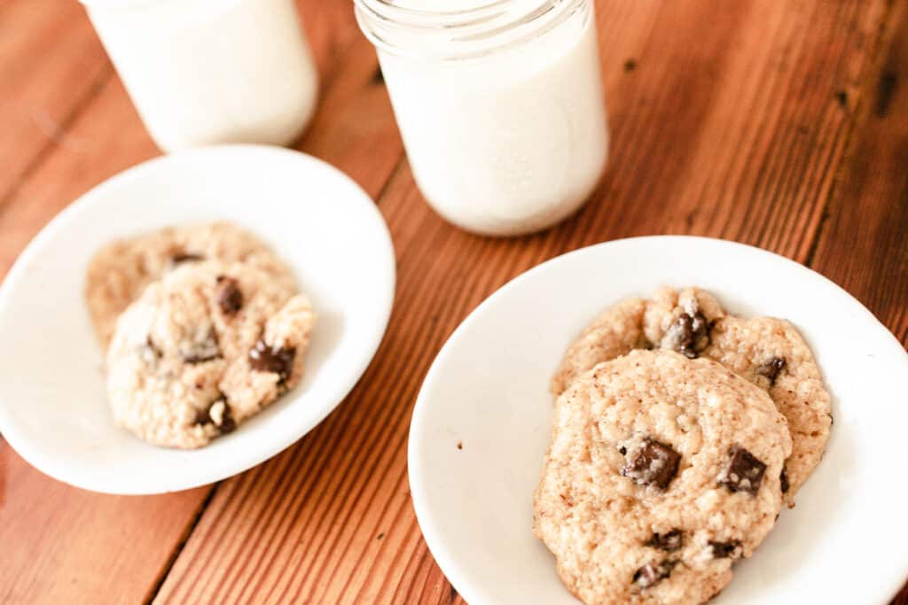two white bowls of sourdough chocolate chip cookies with glasses of milk in the background