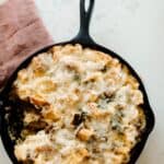 overhead photo of sourdough breakfast strata in a cast iron skillet on a red tea towel on a white quartz countertop